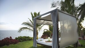 A private outdoor sleeping area with a canopy, a small table with a tray, and a view of the ocean. - Roca Nivaria Gran Hotel (Adeje)