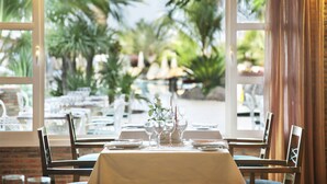 A restaurant with a table set for four, large windows, and a view of palm trees. - Roca Nivaria Gran Hotel (Adeje)