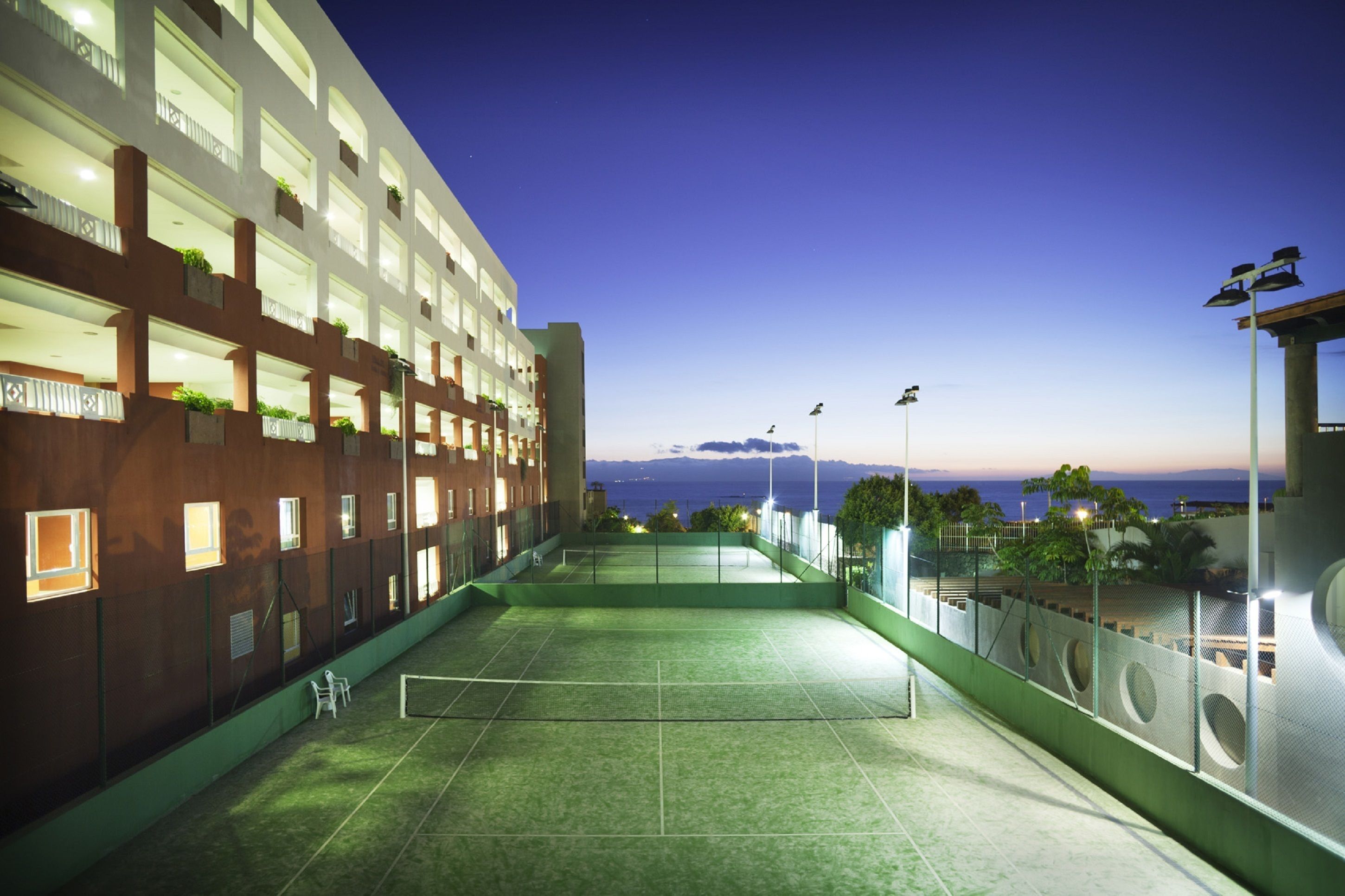 Ein Hallen-Tennisplatz mit Blick auf das Meer im Abenddämmerung.
