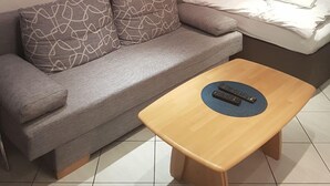 Une chambre moderne avec un canapé gris, une table basse en bois, un lit avec du linge de lit blanc et un tableau au mur.