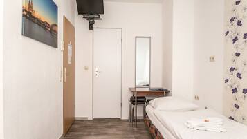 A hotel room with a bed, a desk, a chair, a TV mounted on the wall, and a door.
