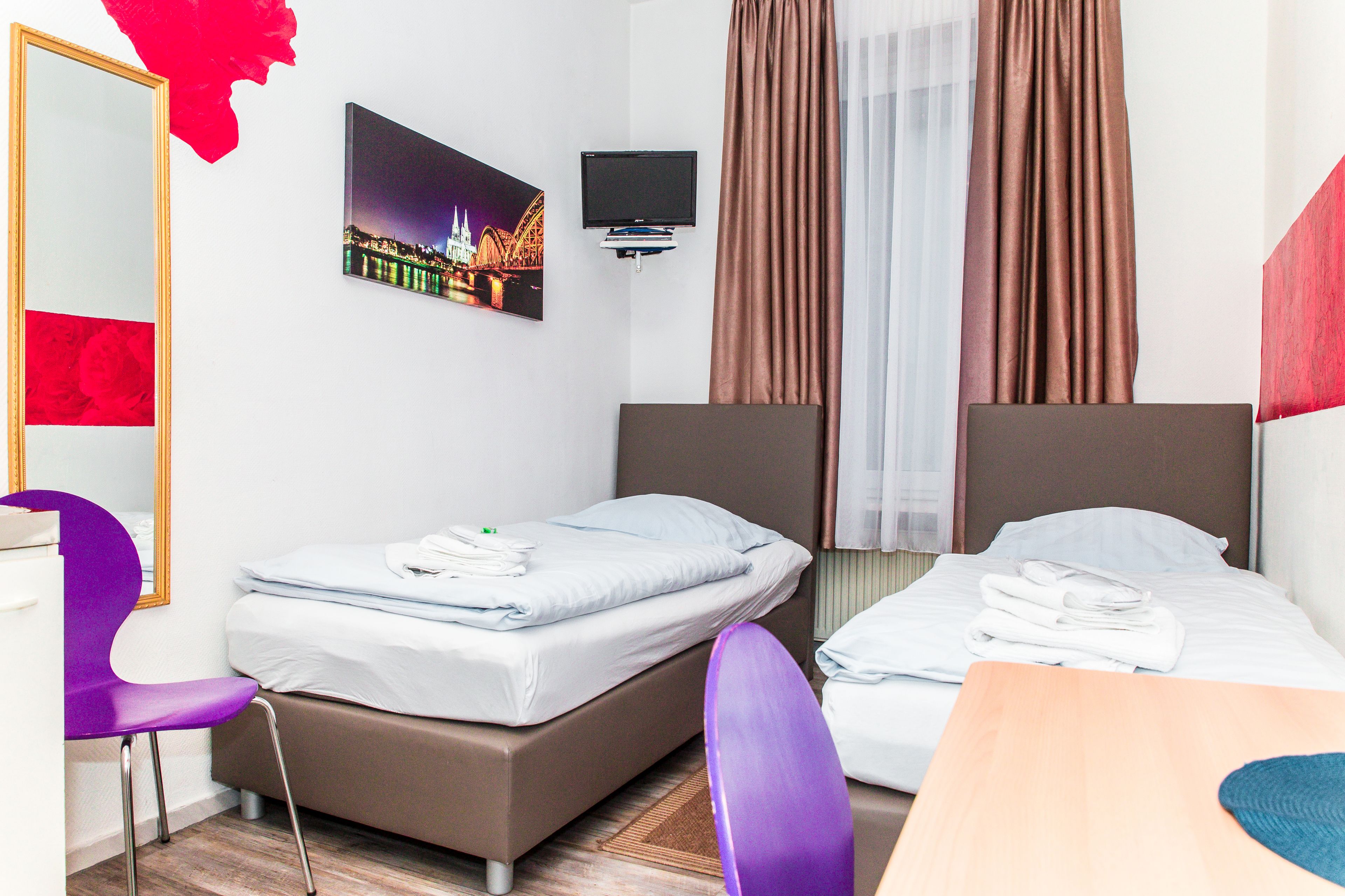 Ein Hotelzimmer mit zwei Betten, einem Fernseher, einem Spiegel und einem Schreibtisch.