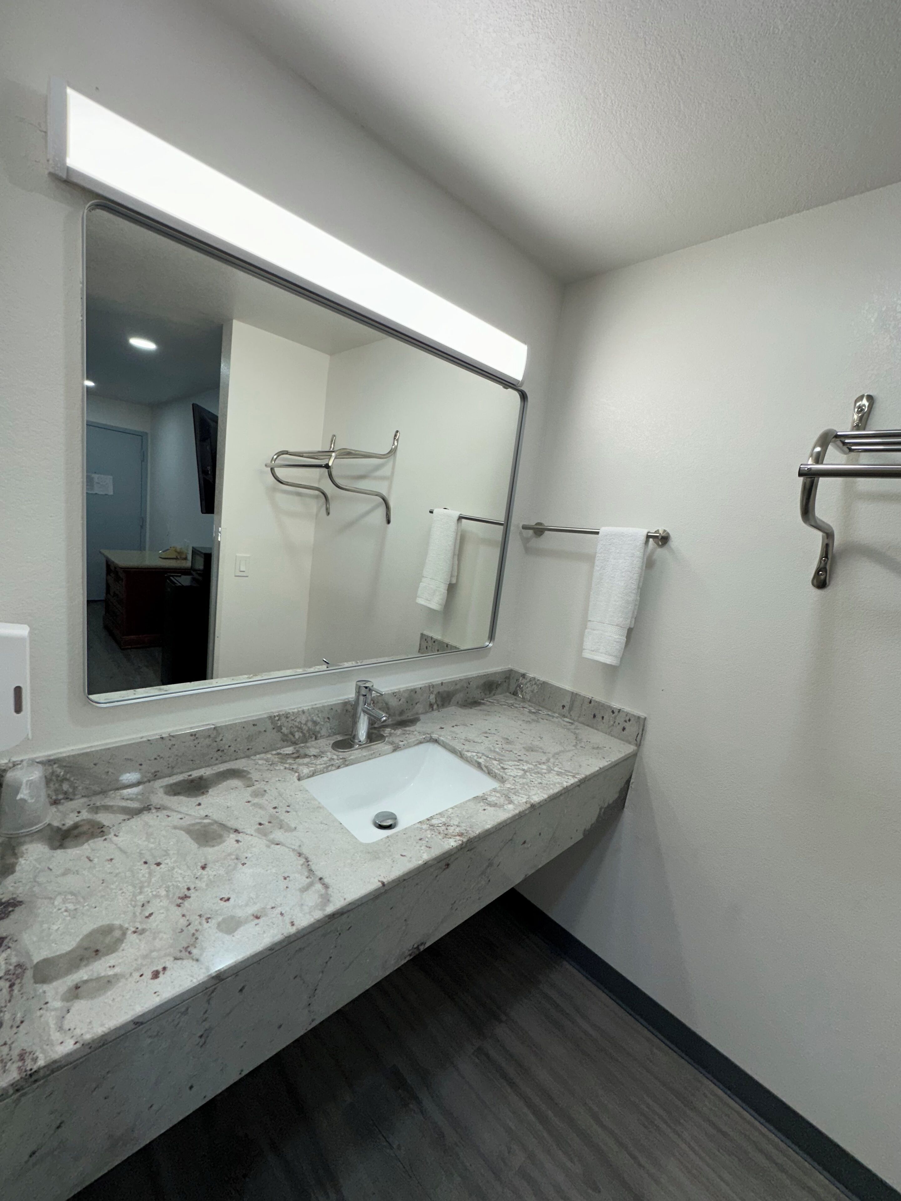 A bathroom with a marble sink, a large mirror, and a towel rack.