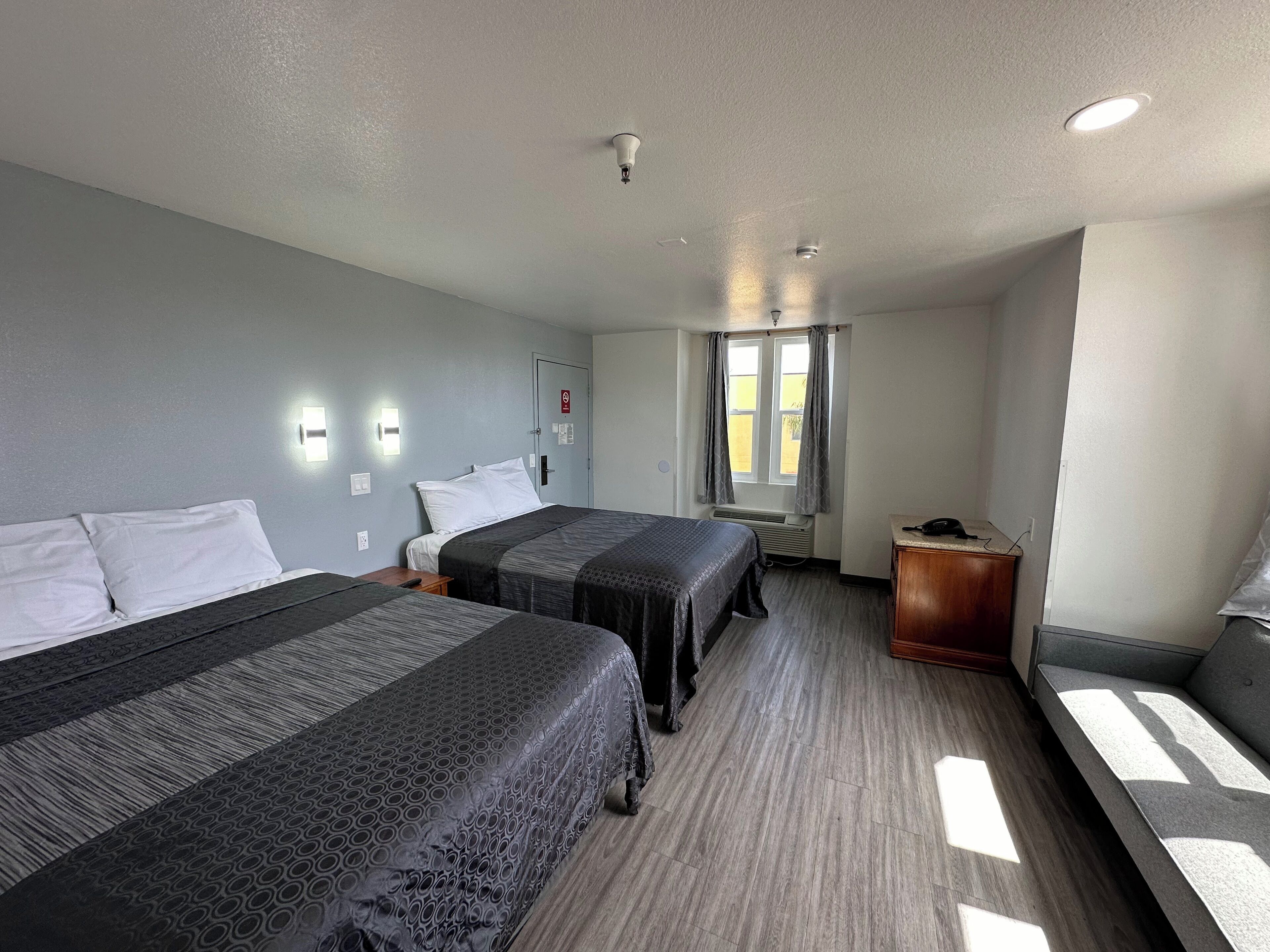 Habitación de hotel con dos camas, un escritorio, una silla, una ventana con cortinas e iluminación en el techo.