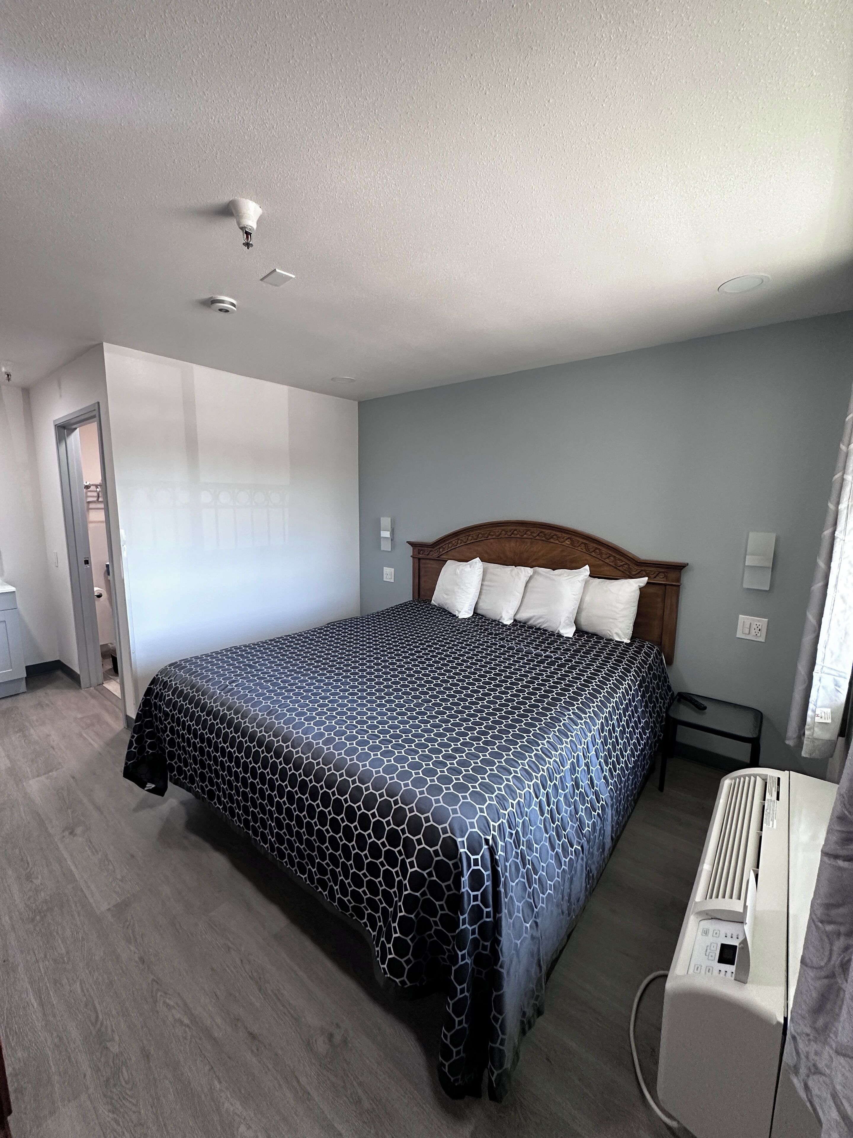 Ein Hotelzimmer mit einem großen Bett, einem hölzernen Kopfteil, einem Nachttisch und einer wandmontierten Klimaanlage.