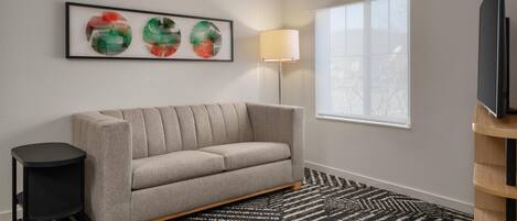 Una sala de estar moderna con un sofá, una obra de arte enmarco, una lámpara de pie y un televisor sobre un mueble.