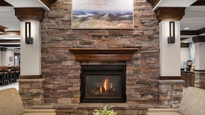A stone fireplace with a fire, a painting above it, and a sofa with a plant in front.