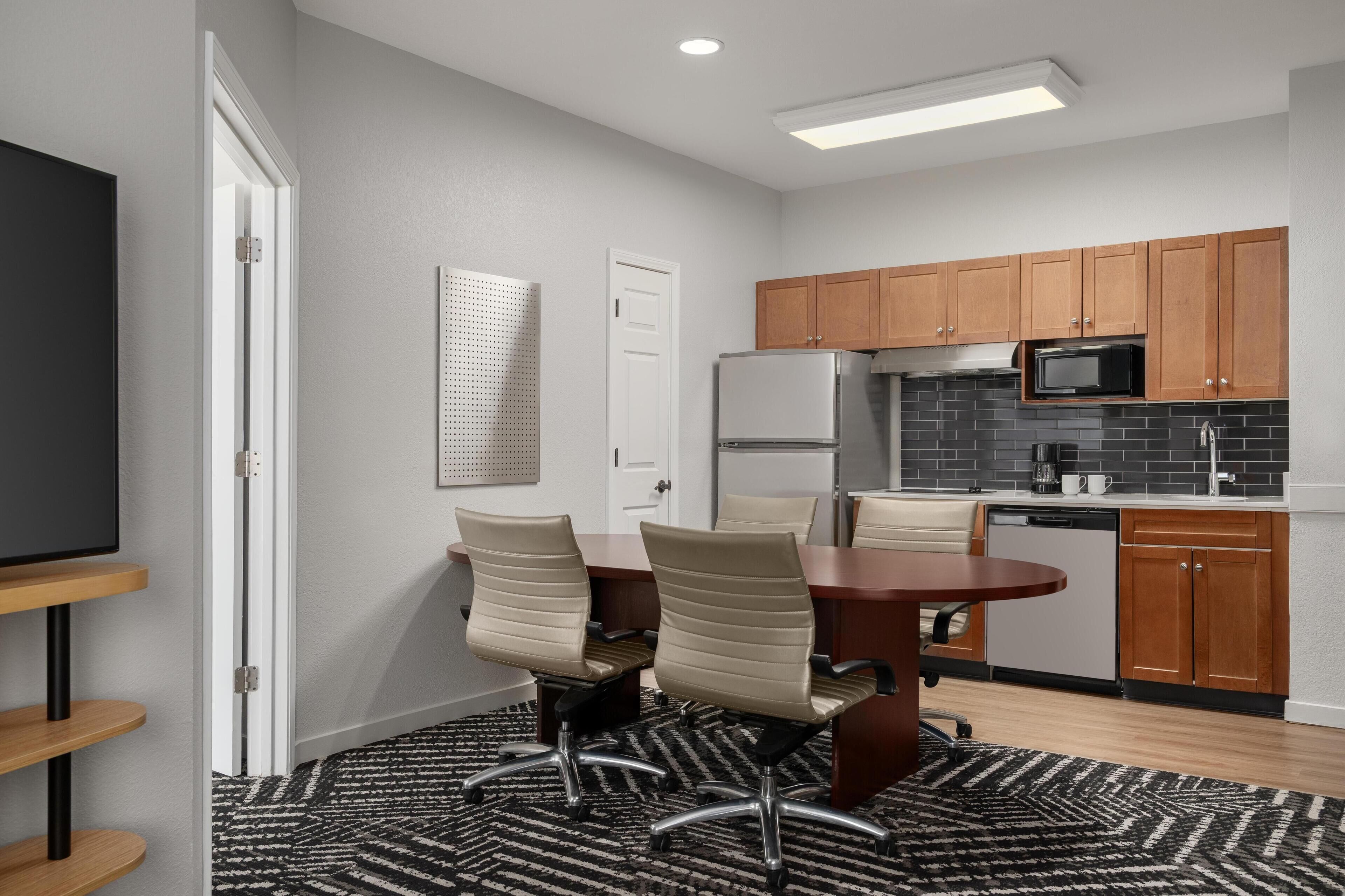 A modern kitchen with wooden cabinets, a refrigerator, microwave, and a dining area with a table and chairs.