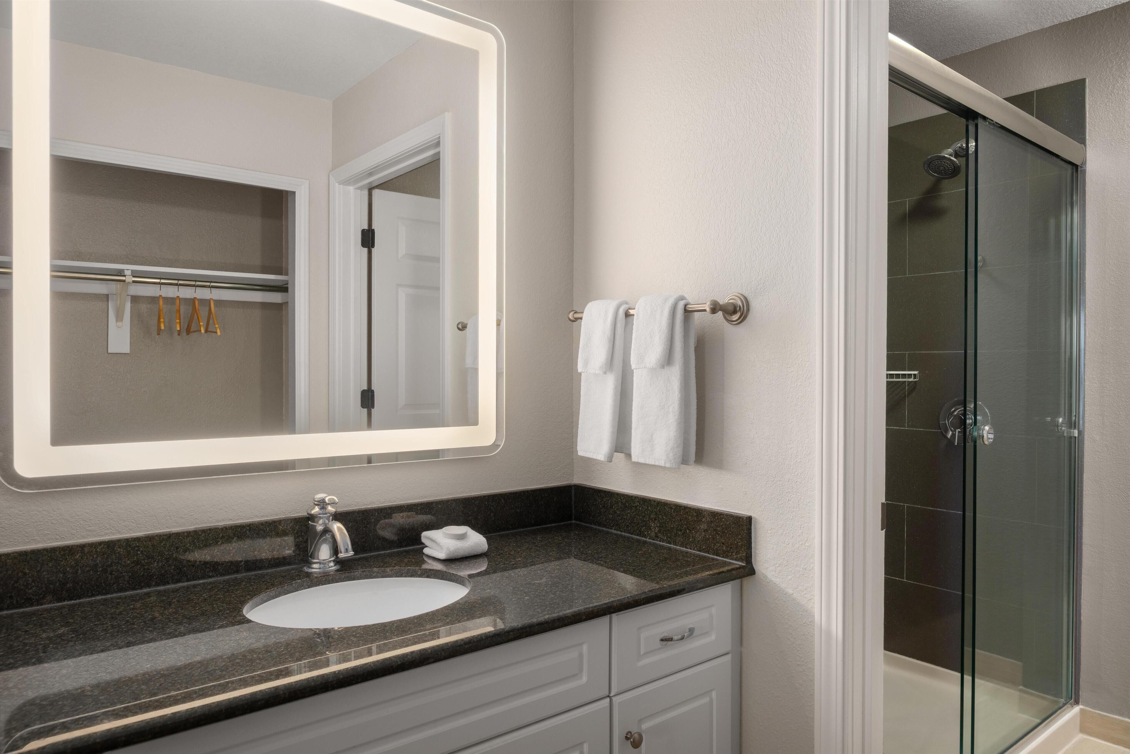 A bathroom with a large mirror, a sink, a glass shower enclosure, and a towel rack.