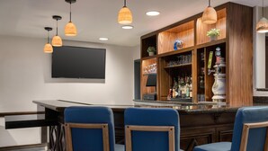 A bar area with wooden cabinets, a flat-screen TV, and blue upholstered chairs.