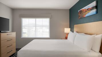A hotel room with a bed, a TV, a dresser, a window, and a painting on the wall.