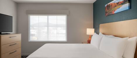 A hotel room with a bed, a TV, a dresser, a window, and a painting on the wall.