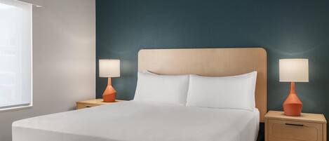 A neatly made bed with white linens, two bedside tables with lamps, and a dark teal accent wall.