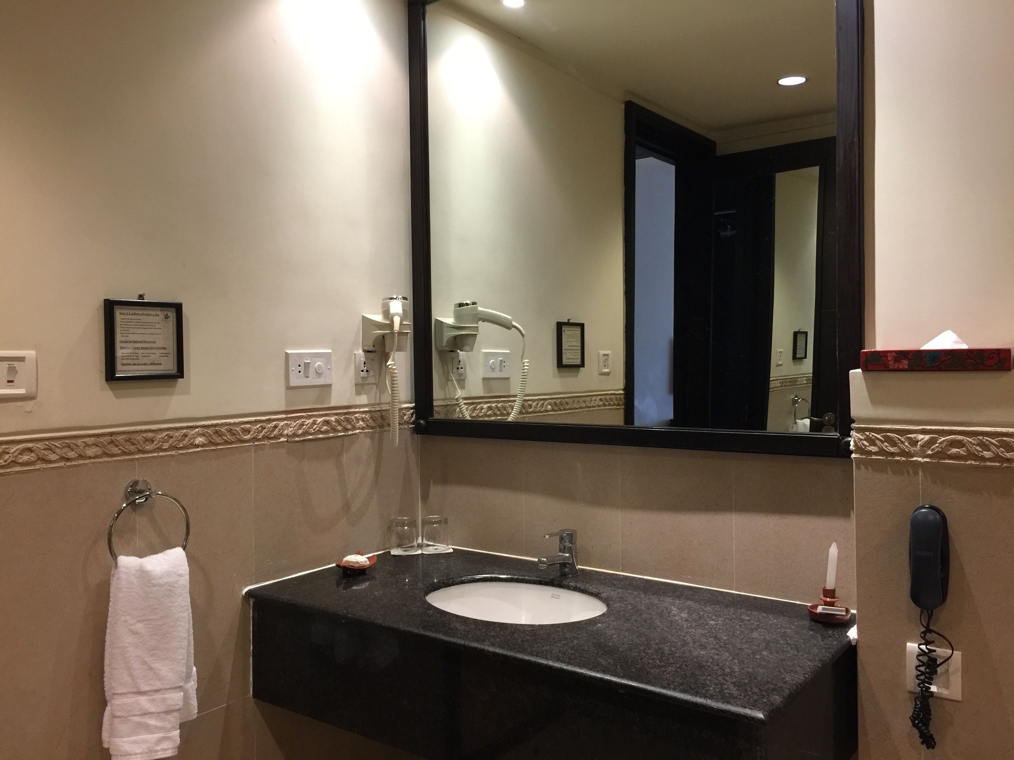 A bathroom with a black countertop sink, a mirror, a towel rack, a hairdryer, and a phone.