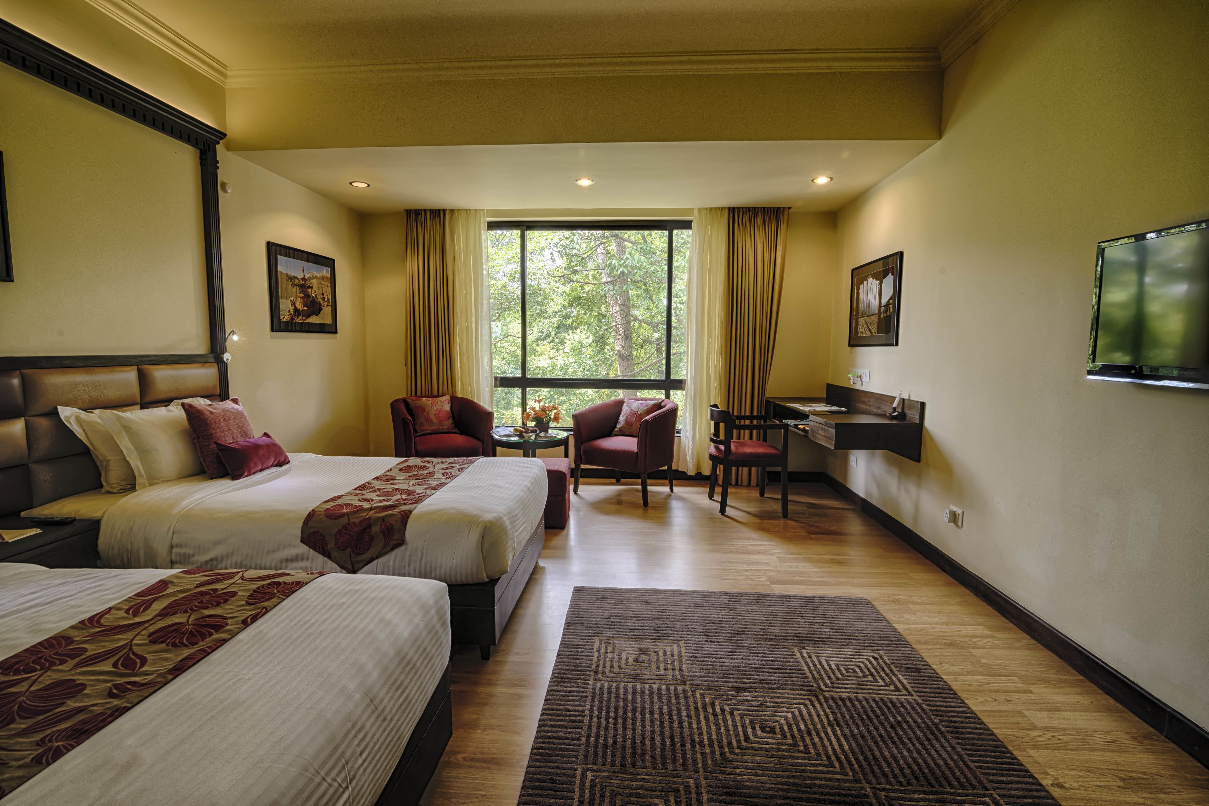 Habitación de hotel con dos camas, un escritorio, una silla y un televisor en la pared.