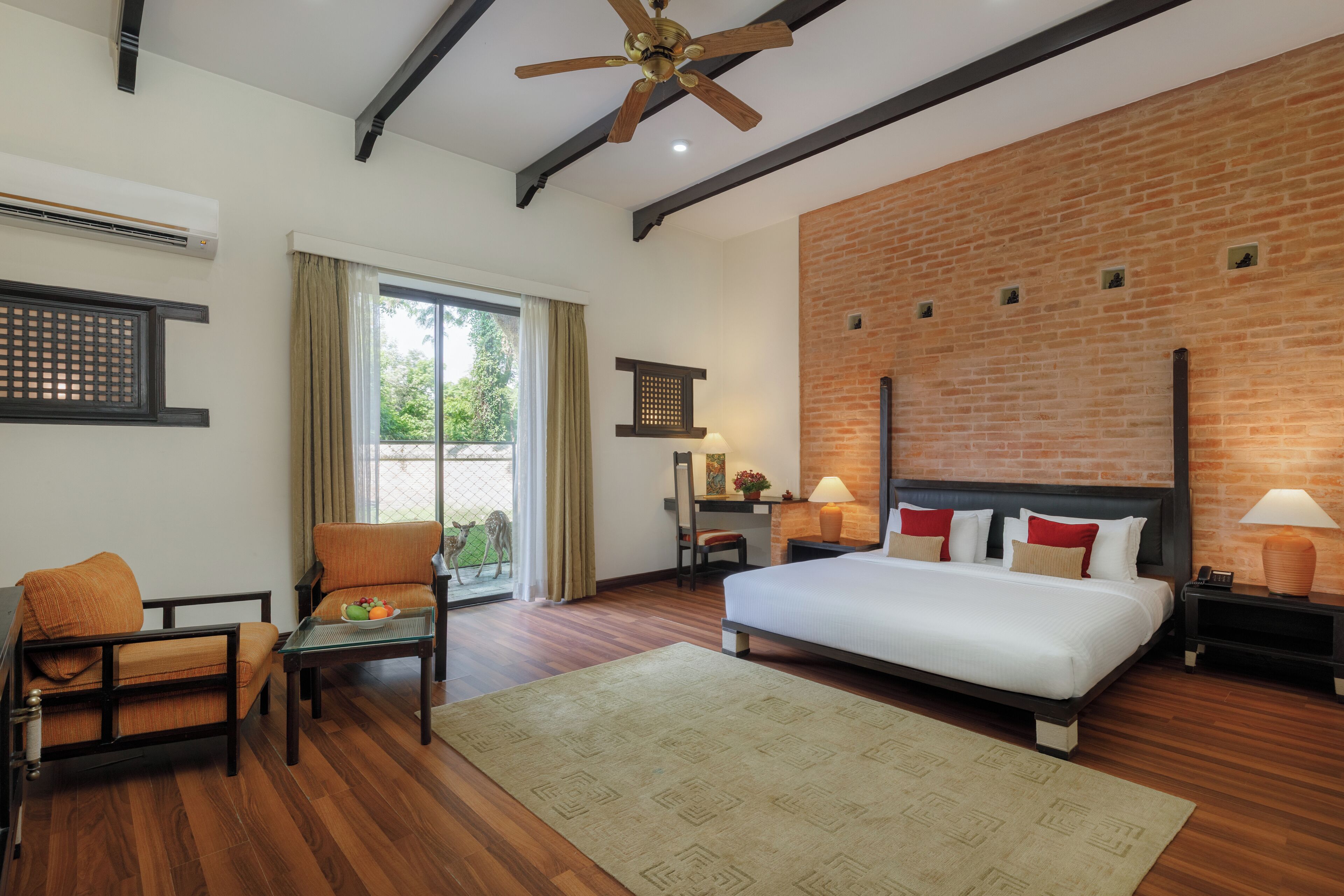 A modern hotel room with a large bed, a seating area with a table, a ceiling fan, and a brick accent wall.