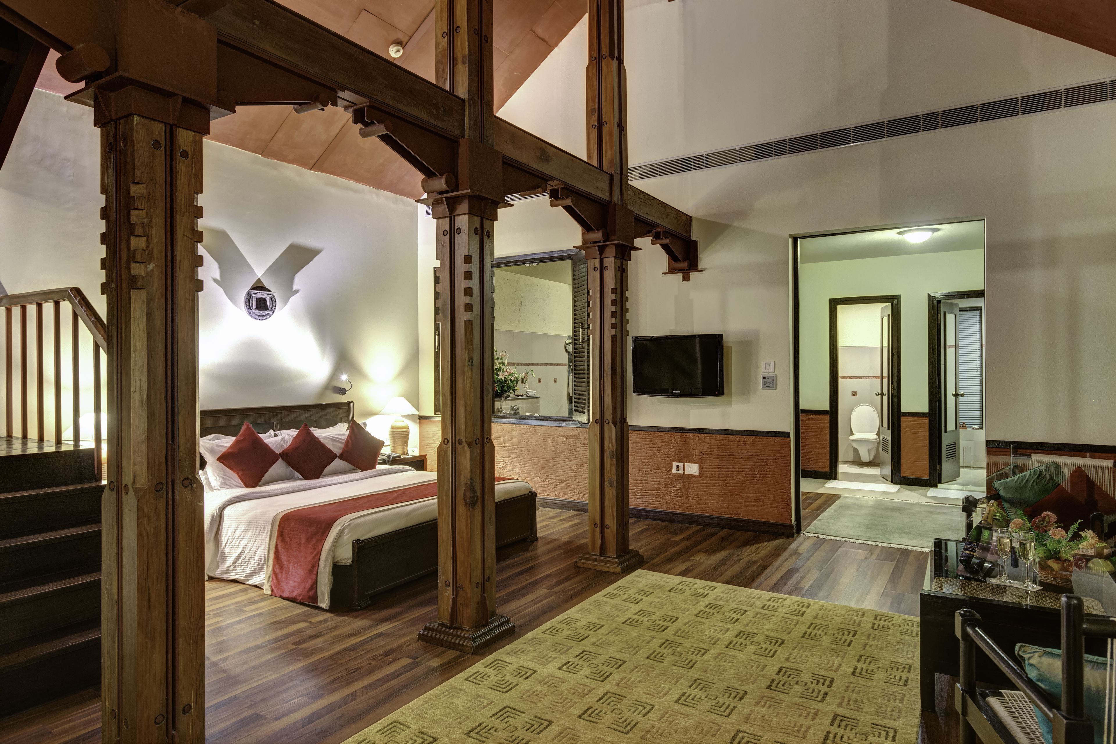 Ein Hotelzimmer mit einer Holztreppe, einem großen Bett mit roten Kissen, einem Flachbildfernseher und einem durch eine offene Tür einsehbaren Badezimmer.