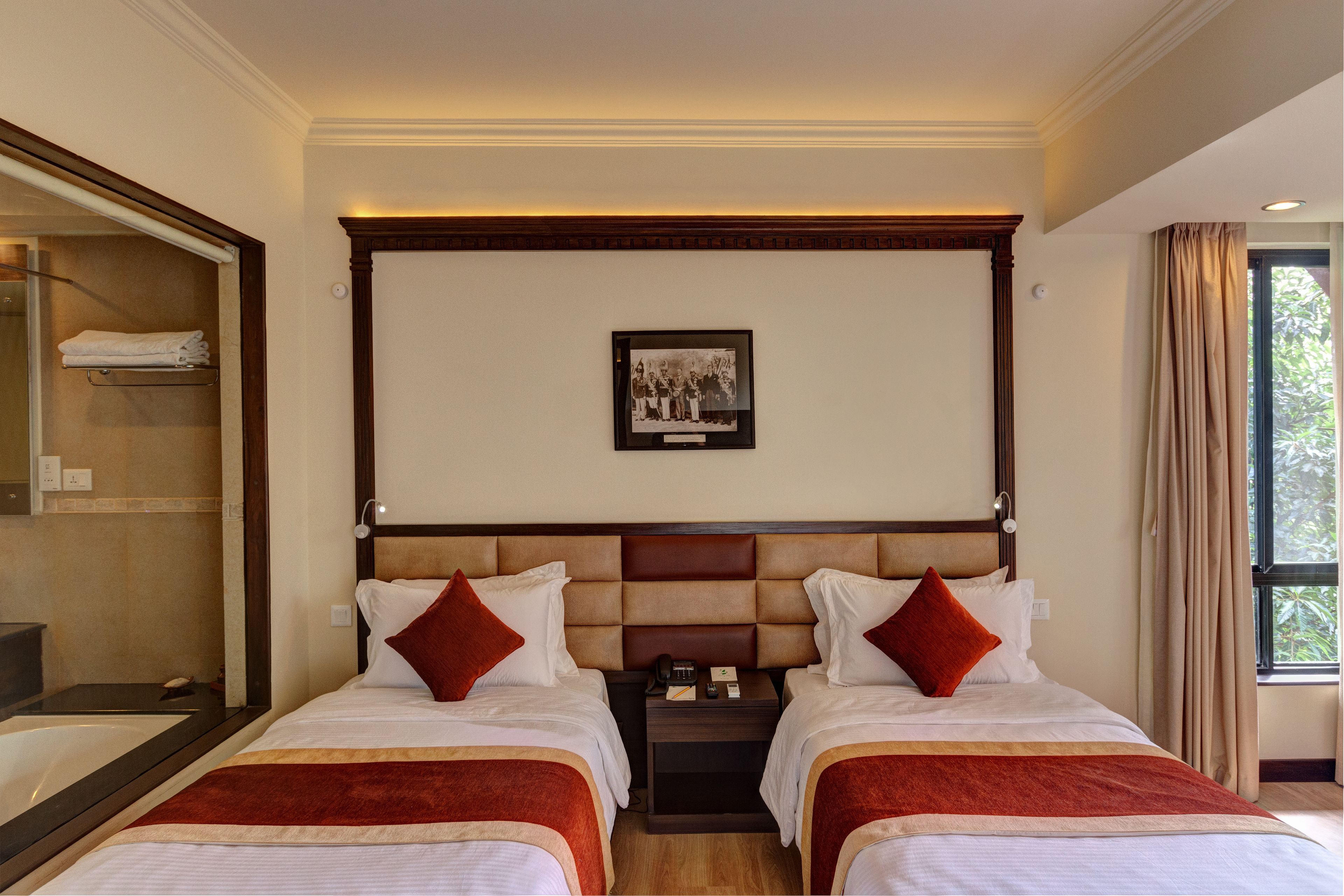 Une chambre d’hôtel avec deux lits, un grand miroir, une photo encadrée accrochée au mur et une fenêtre avec des rideaux.