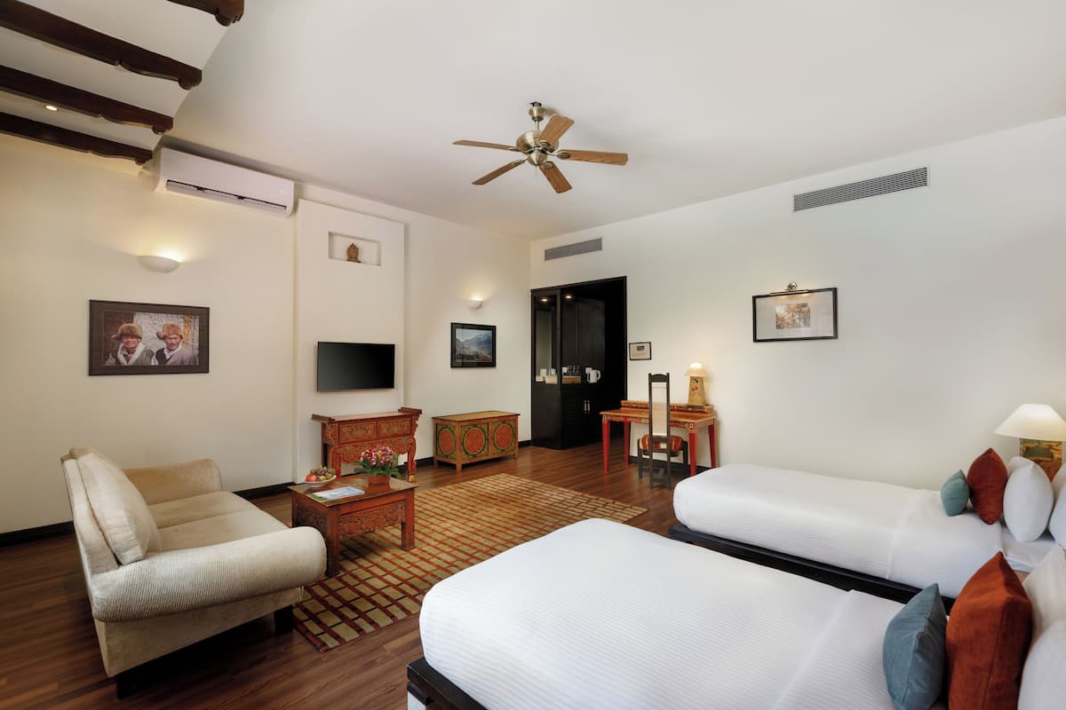 Ein Hotelzimmer mit einer Couch, zwei Betten, einem Schreibtisch, einem Fernseher und einem Deckenventilator.