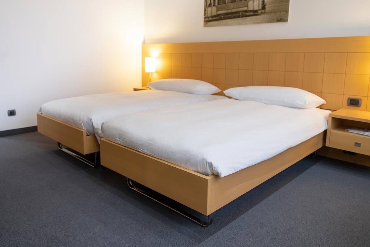 Una cama doble con estructura de madera, dos mesitas de noche y una lámpara de pared.