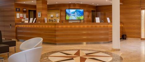 A reception area with a wooden reception desk, a large flat-screen TV, and a geometric floor design.
