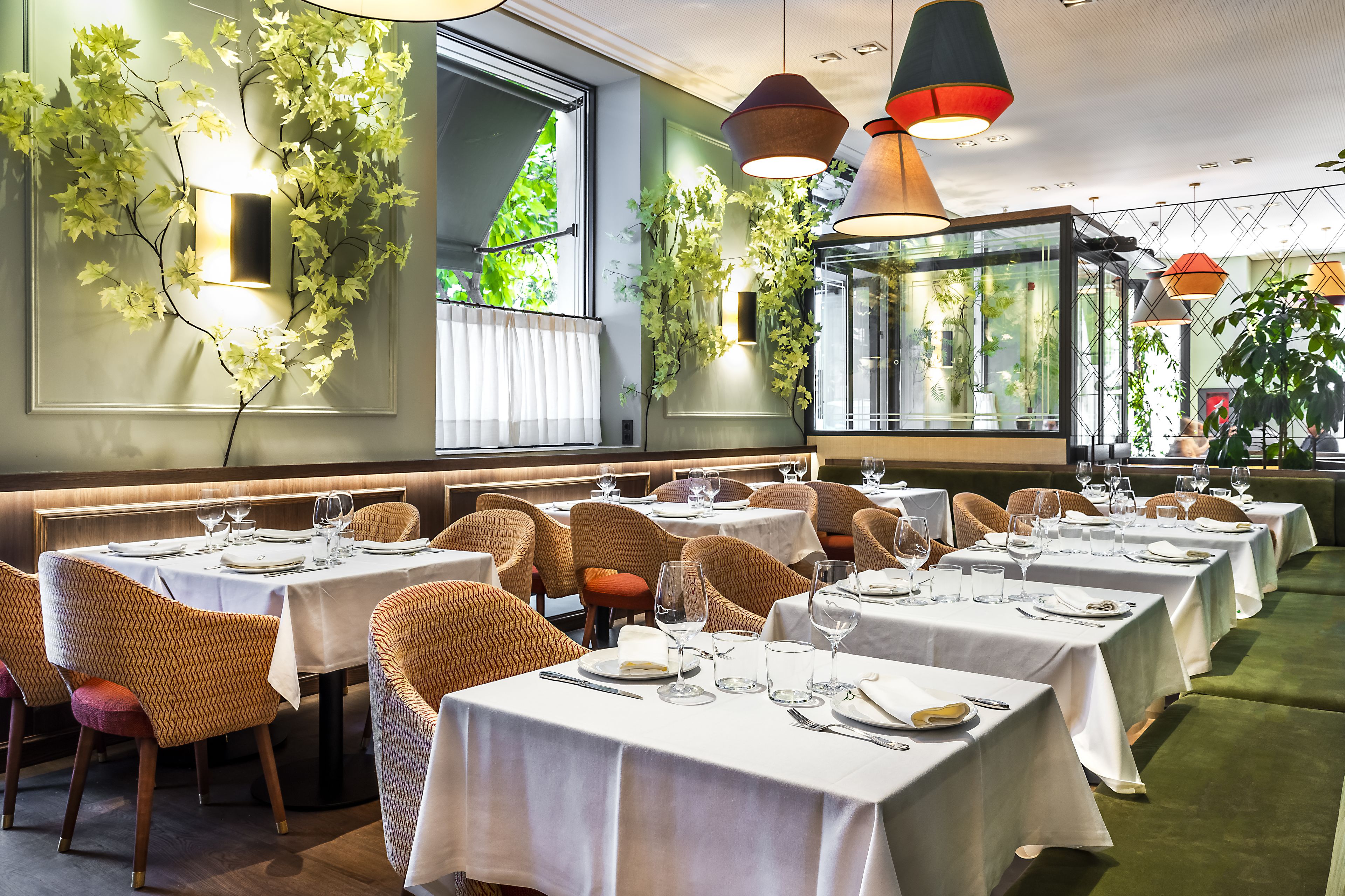A restaurant with multiple tables set for dining, wicker chairs, and hanging pendant lights.