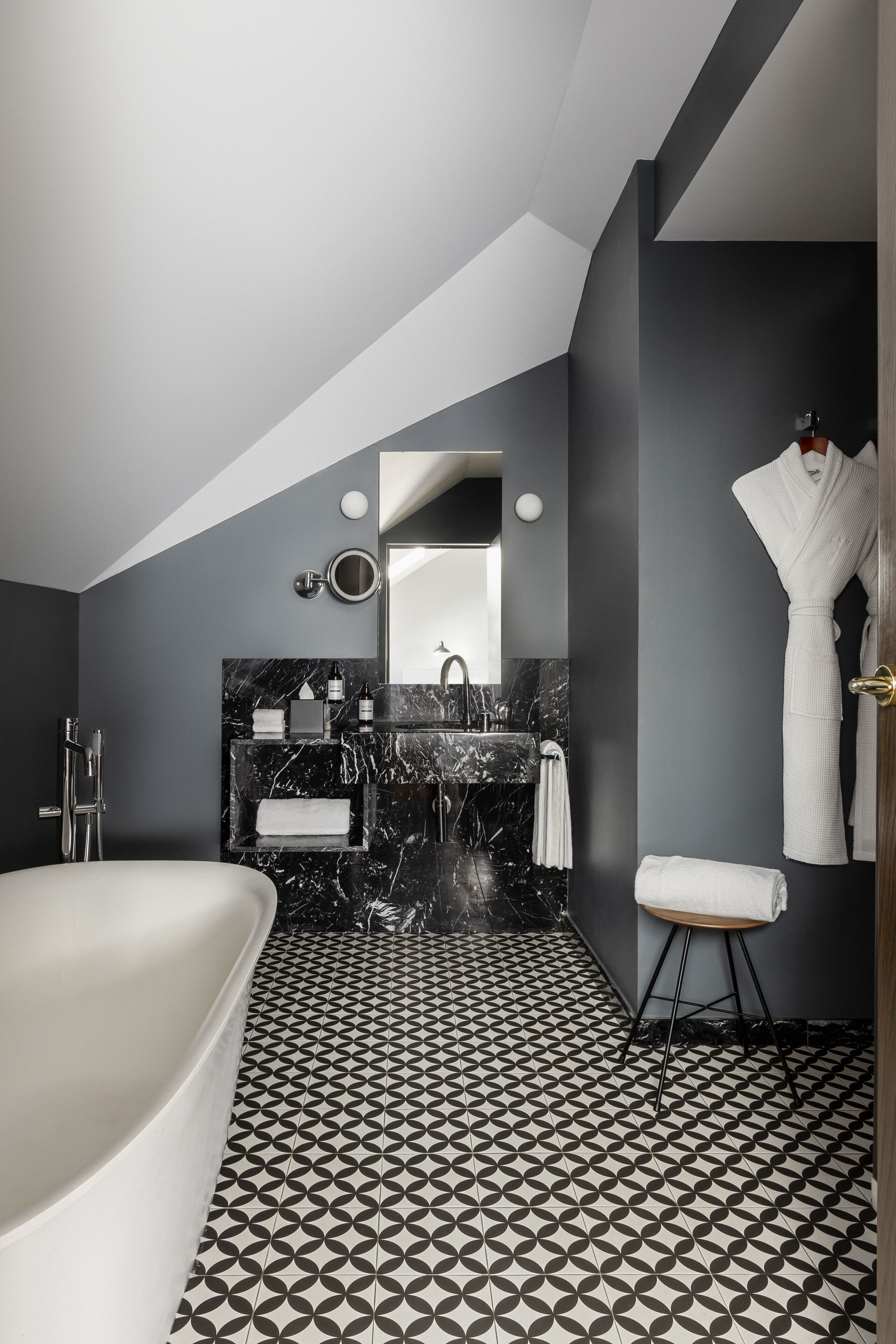 Un baño moderno con una bañera independiente, un tocador de mármol y un suelo con estampado geométrico.