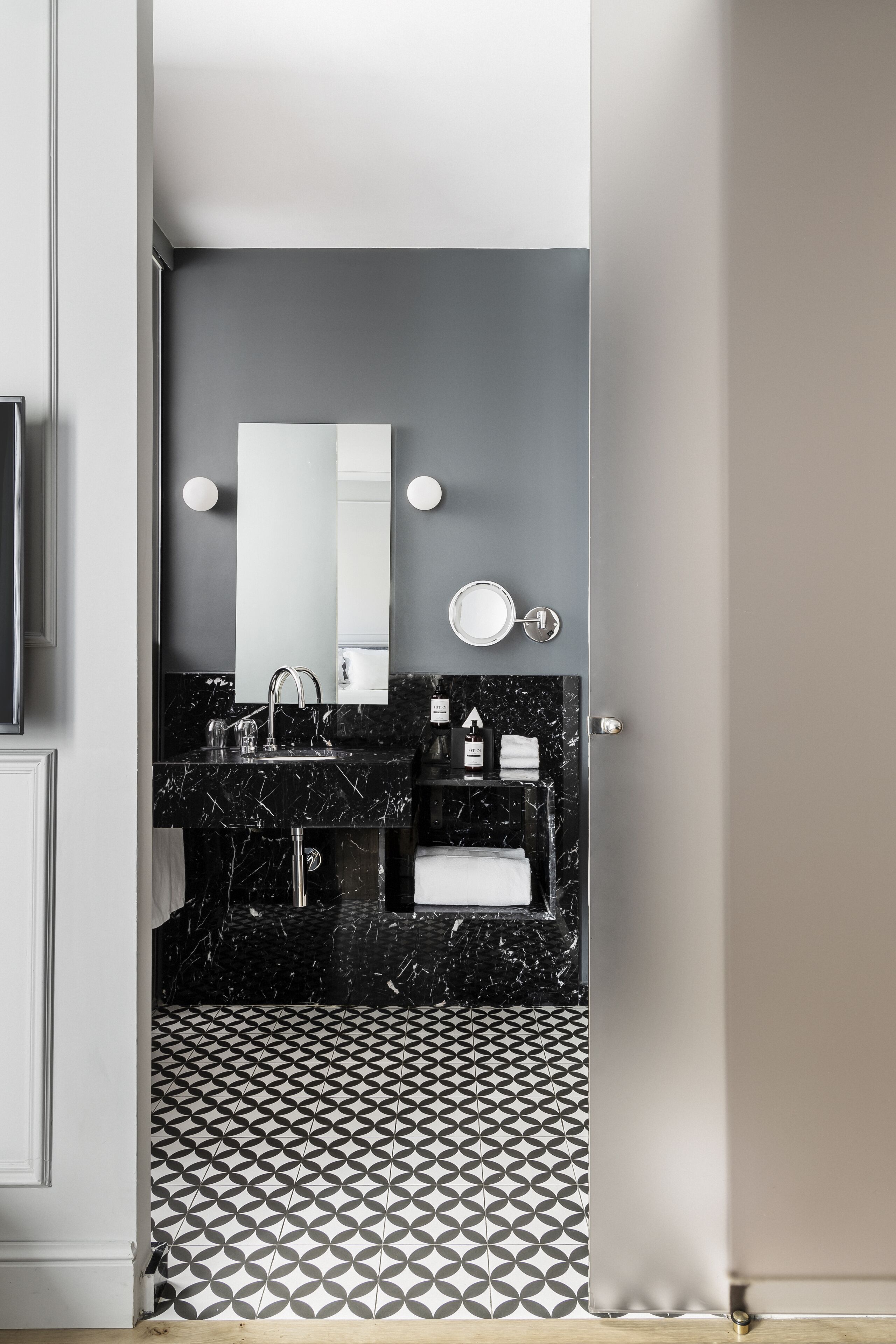 A modern bathroom with a black marble sink, a large mirror, and a geometric patterned floor.