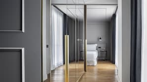 Passadís d'hotel modern amb sòl de fusta, un llit blanc i una taula petita amb una làmpada.
