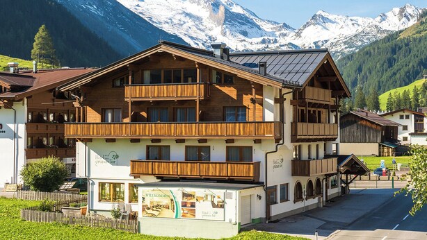 Un hotel de varios pisos con balcones de madera y un paisaje montañoso al fondo.