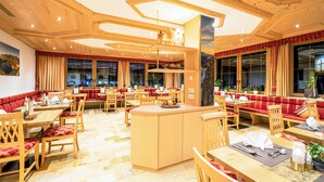 Un restaurante con mobiliario de madera, asientos acolchados rojos y ventanas grandes con cortinas.