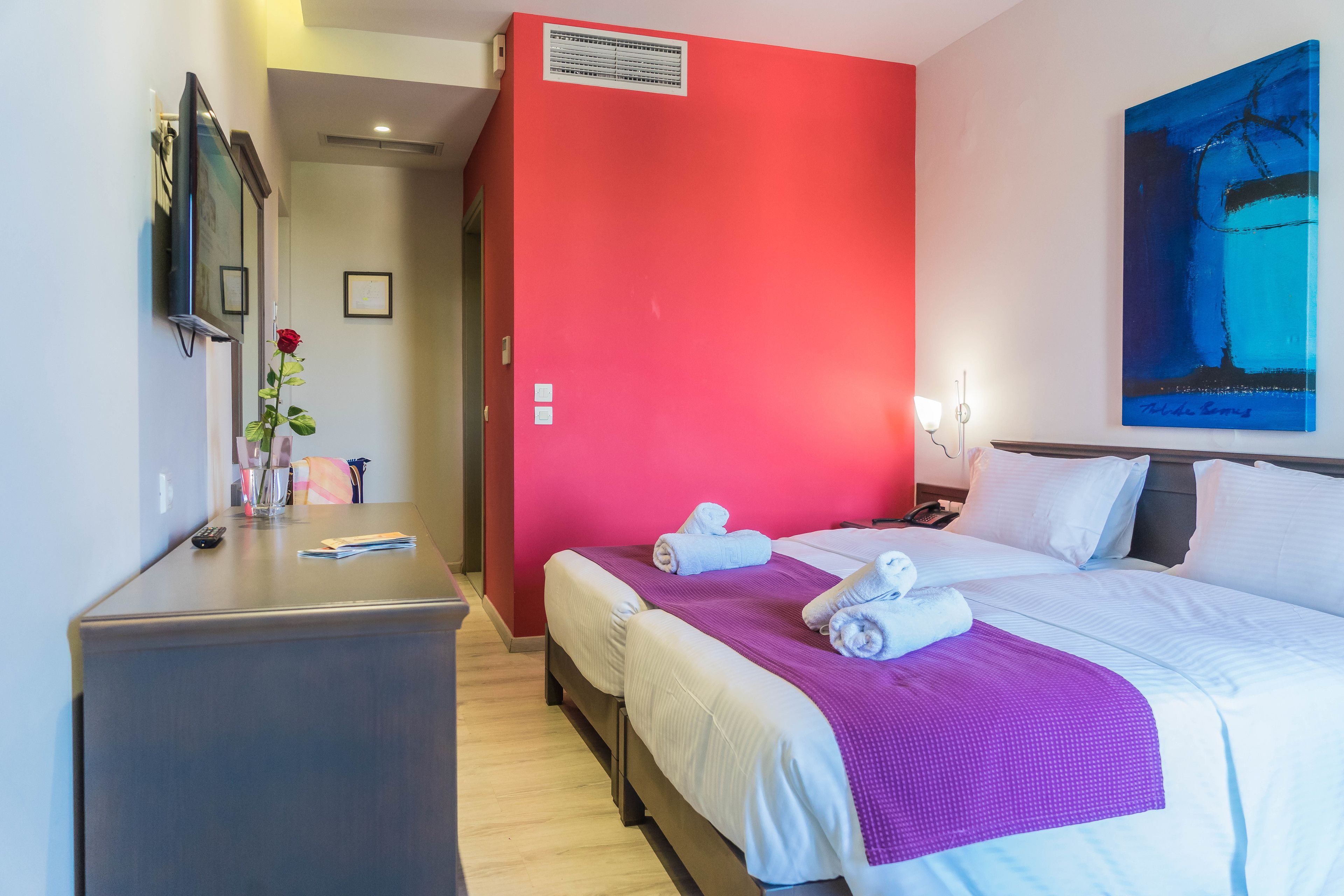 A hotel room with two beds, a desk, a TV, and a painting on the wall.