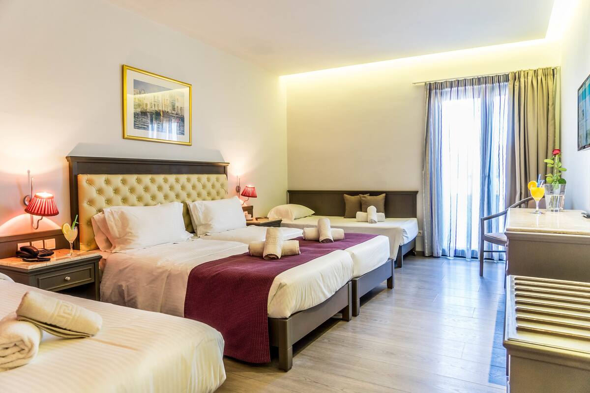 Habitación de hotel con dos camas, un escritorio y una silla. Hay lámparas en las mesitas de noche, un cuadro en la pared y una ventana con cortinas.