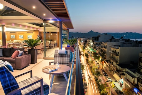 A modern hotel balcony with seating, a table, and a view of the cityscape.