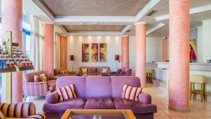 Um hall amplo com um grande sofá roxo, poltronas listradas e uma mesa de centro de vidro.