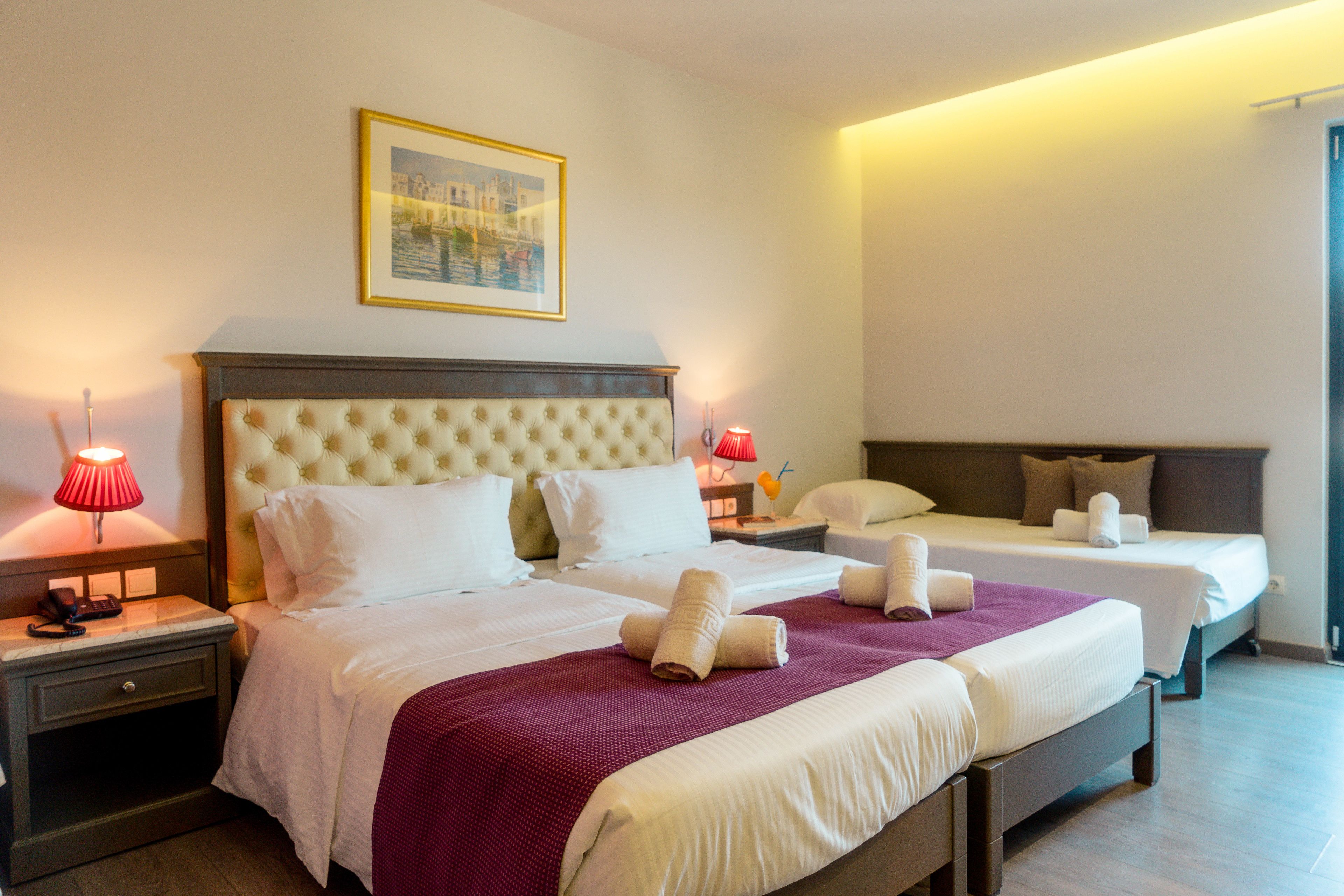 A hotel room with two beds, a large headboard, and a framed picture on the wall.