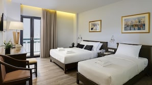 Quarto de hotel com duas camas, uma mesa com luminária, uma cadeira e vista para o exterior.