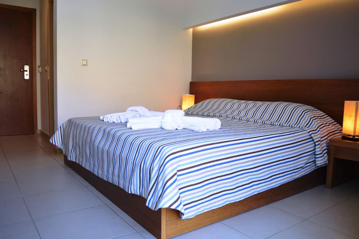 Una cama bien tendida con ropa de cama a rayas, un cabecero de madera y una lámpara de noche.
