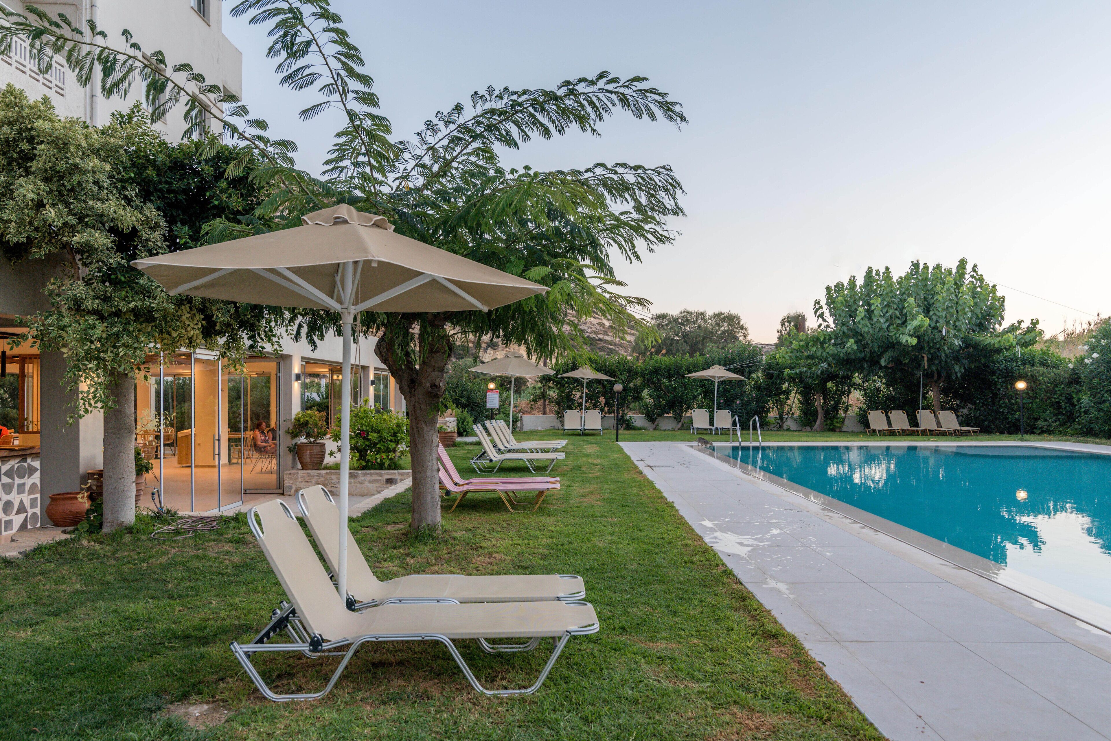 A poolside area with lounge chairs and umbrellas, a pool, and a building with a glass door entrance.