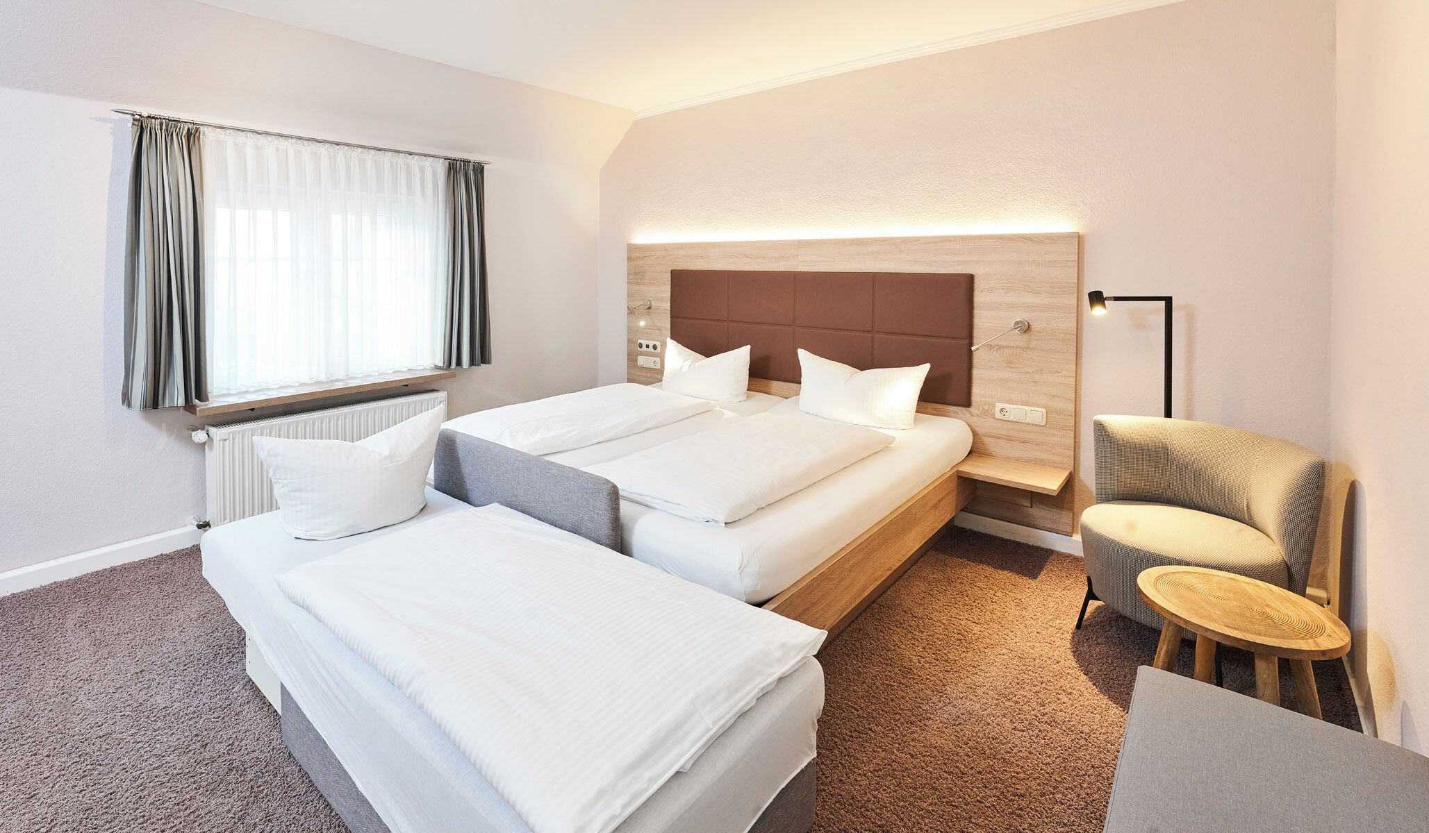 Ein Hotelzimmer mit zwei Betten, einem Nachttisch, einem Sessel und einer Lampe.
