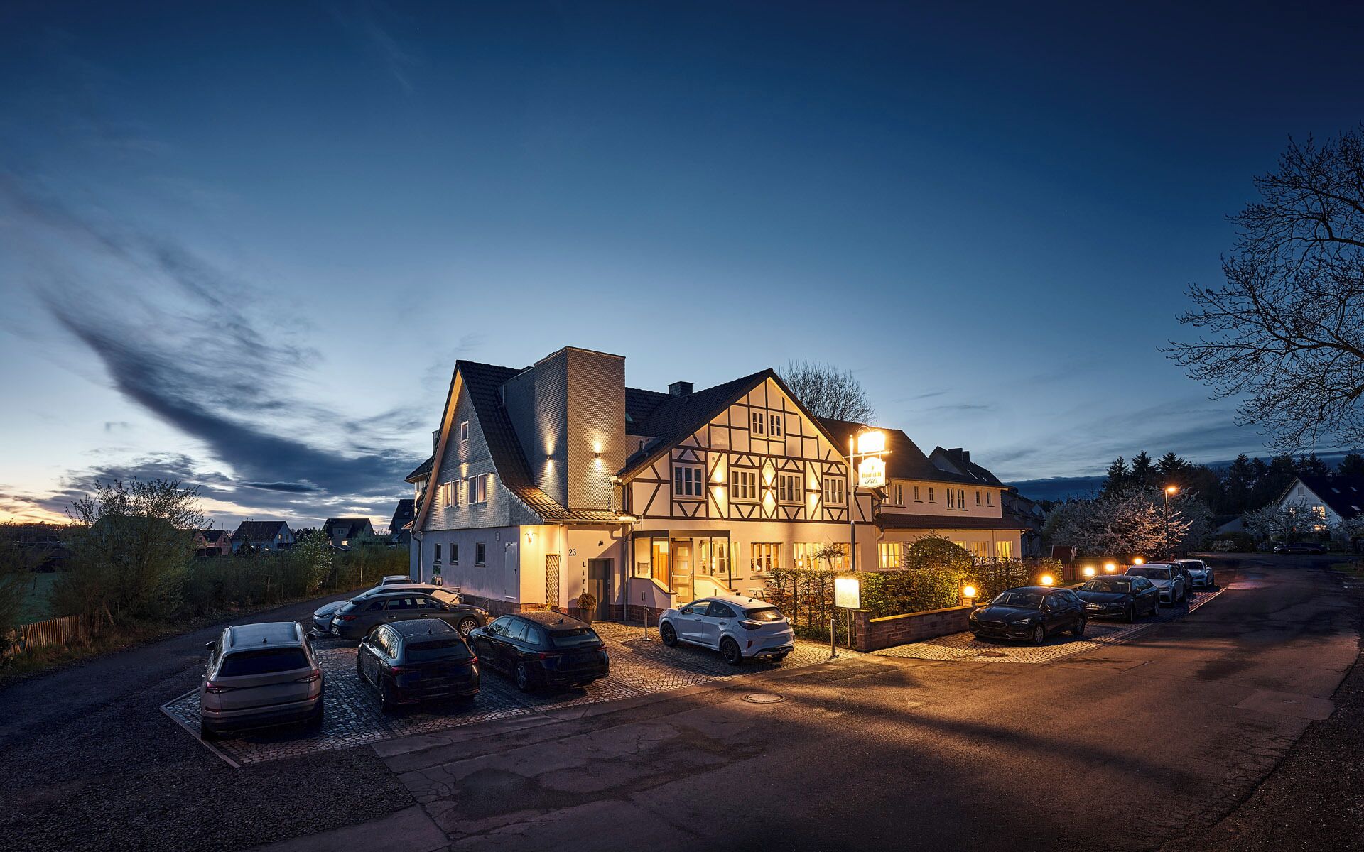 A traditional half-timbered building with a driveway and parked cars.