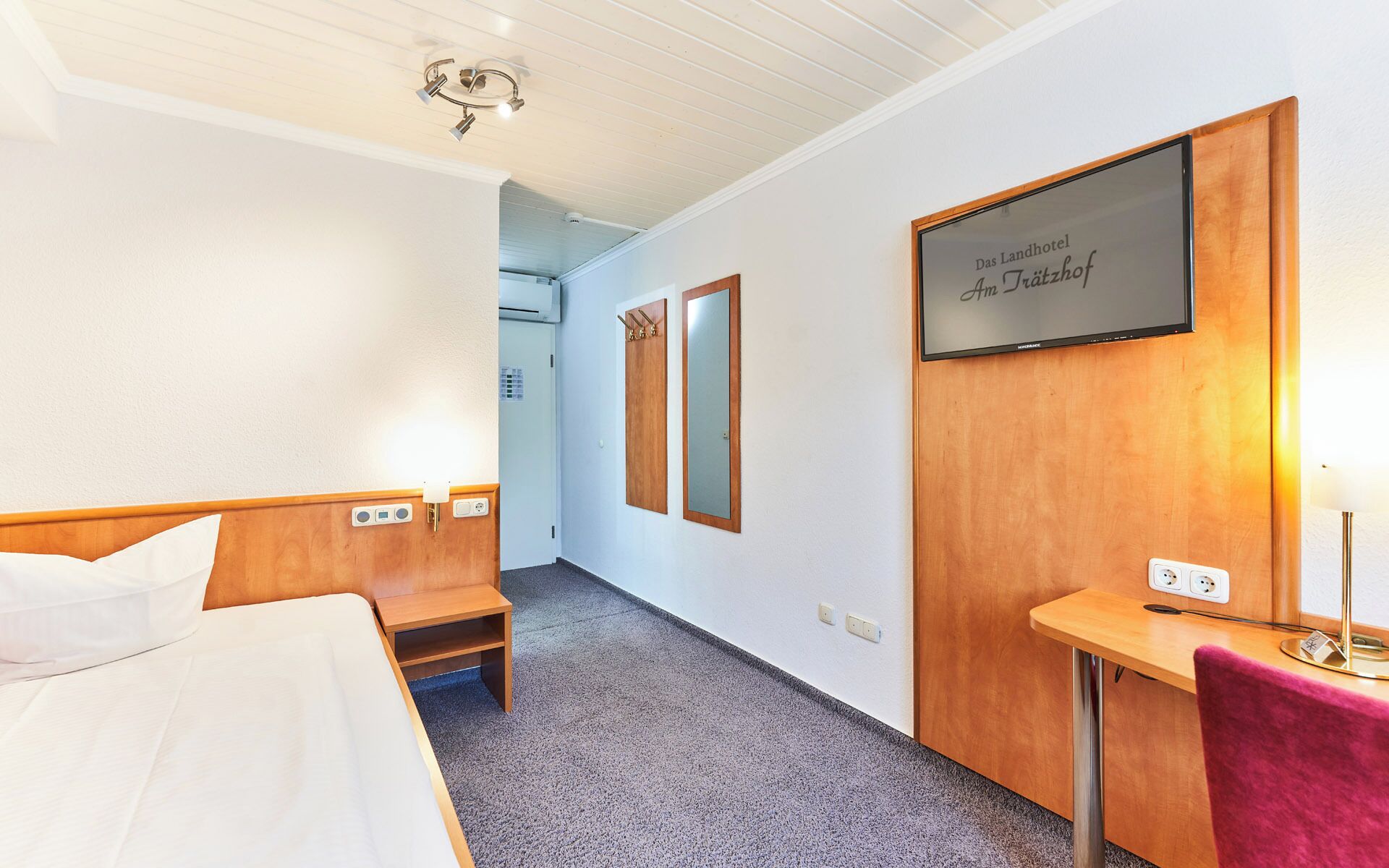 A hotel room with a bed, a small table, a mirror, and a sign on the wall.