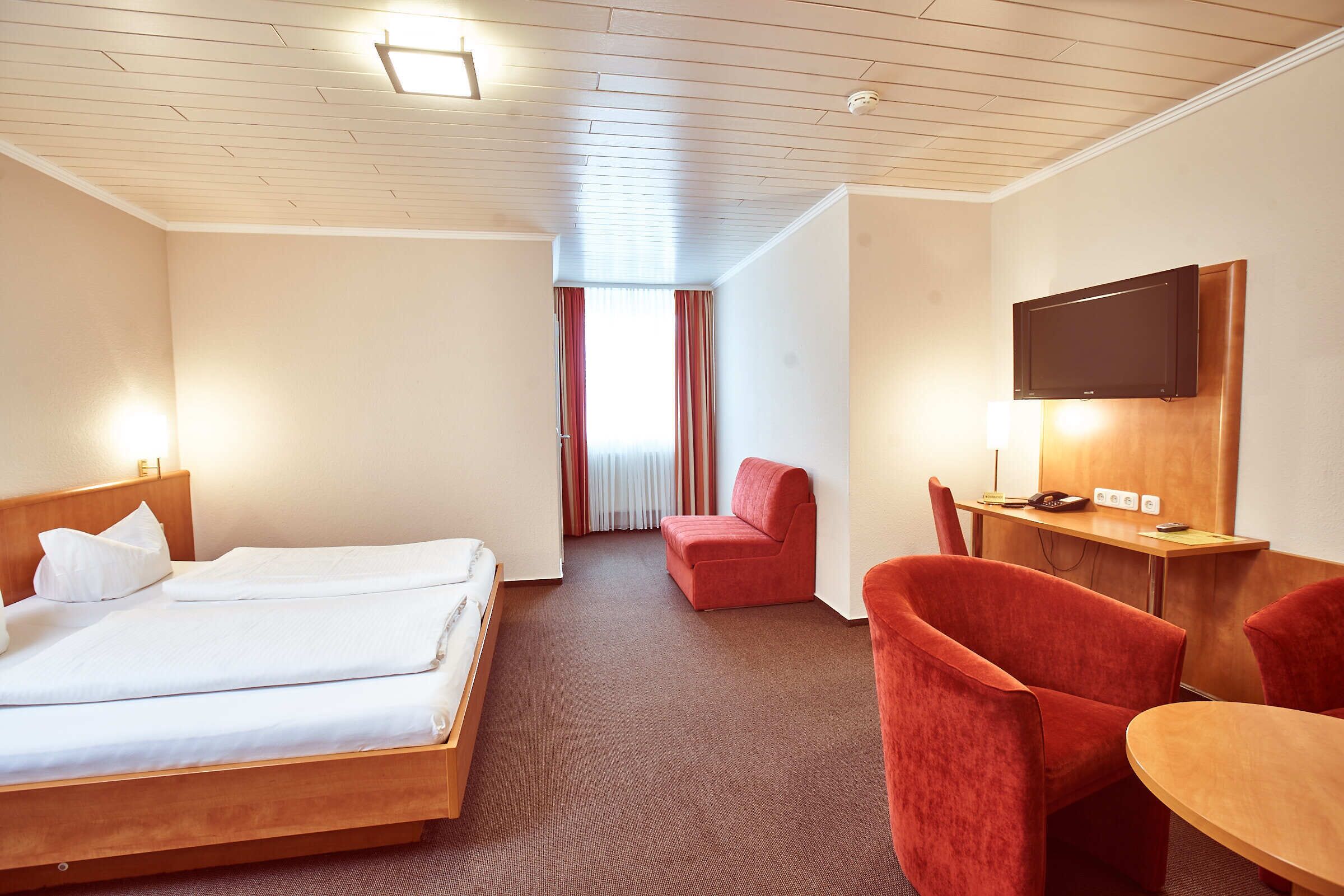 Ein Hotelzimmer mit einem Bett, einem Schreibtisch mit Fernseher und einem roten Sessel.