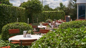 An outdoor dining area with round tables and wooden chairs, surrounded by greenery. - Das Landhotel Am Trätzhof (Fulda)