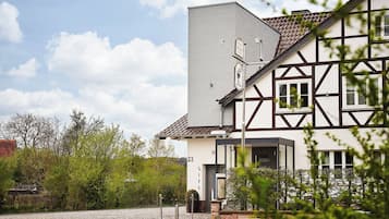 Une maison traditionnelle à colombages agrémentée d’une extension moderne, une allée pavée et une végétation luxuriante.