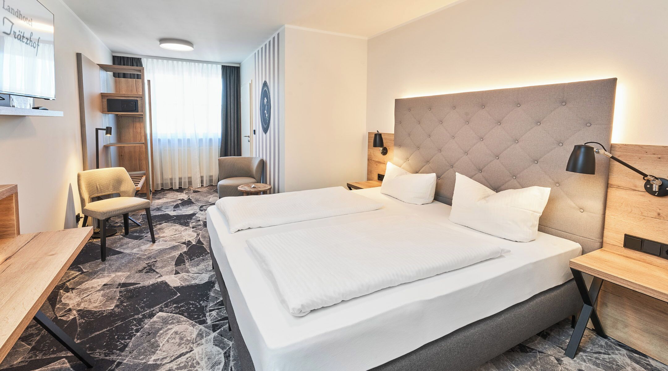 A hotel room with a large bed, two bedside tables, a desk, a chair, a TV, and a wardrobe.