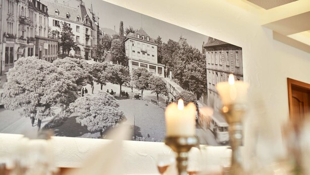 A dining area with a mural of a snowy landscape, a candle on the table, and a view of the cityscape through the window. - Das Landhotel Am Trätzhof (Fulda)