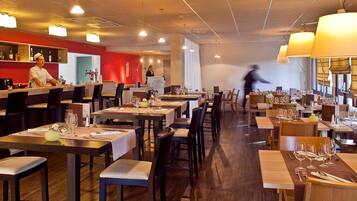 Un restaurant doté de plusieurs tables, de chaises et d’un bar où sont exposées des bouteilles.