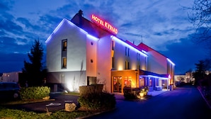 A modern hotel with a neon sign, a well-lit entrance, and a parking area.
