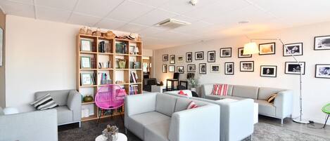 Un salon moderne avec des canapés gris, une table basse blanche et une bibliothèque remplie de livres et d’objets décoratifs.
